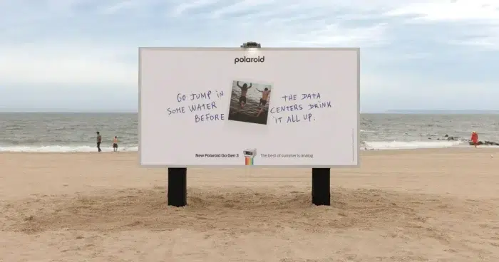 Affiche d'une campagne Polaroïd sur une plage, face à l'eau. On peut y lire : Plonge profiter de l'eau avant que les data-centers l'aient toute bu 
